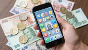 Mão segurando celular com ícones de aplicativos e dinheiro.