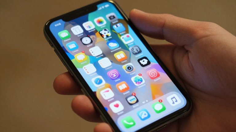 Mão segurando celular com ícones de aplicativos populares na tela.